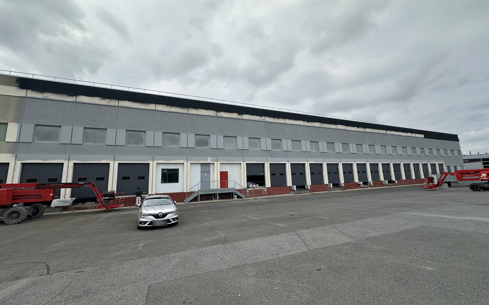 Long bâtiment logistique en cours de mise en peinture, deux nacelles devant les quais